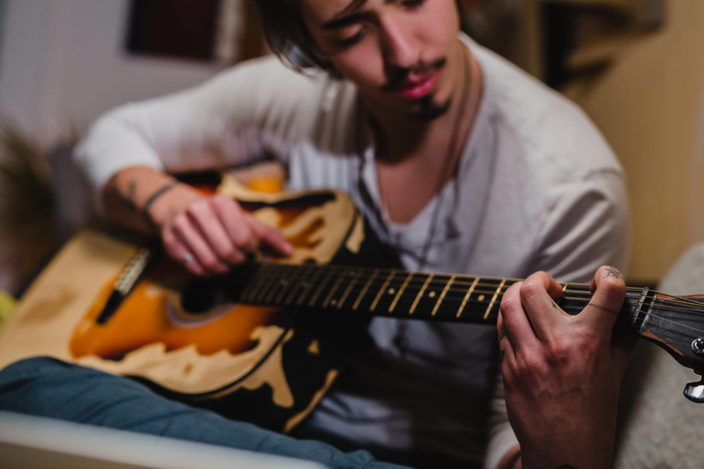 A young man practices guitar at home, focusing on his technique, reflecting how online music learning builds confidence and performance skills
