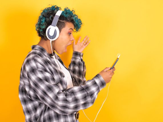Music fan wearing headphones reacting excitedly to content on a smartphone. 