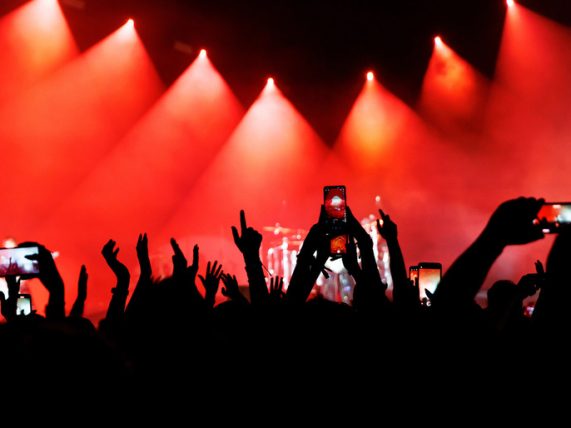 Crowd at a live concert holding up phones to record short clips, with bright stage lights highlighting a moment designed for quick, shareable viewing.