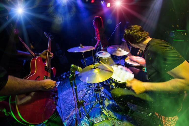 A live band performing on stage with vibrant lights and a drummer in action.