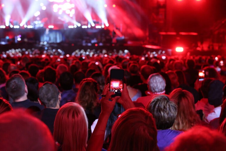 Crowd of fans recording a live concert with bright red stage lights during a Harry Styles performance.