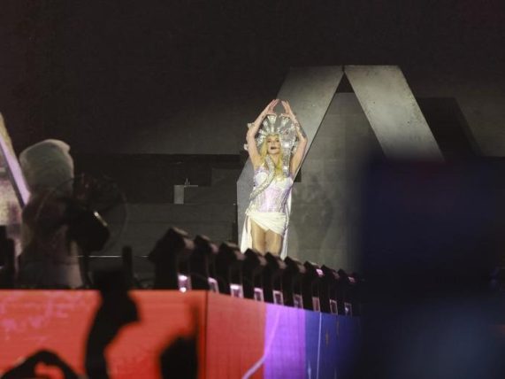 A live concert performance with a singer on stage under bright stage lighting, facing an audience, capturing the atmosphere of a major music event. 