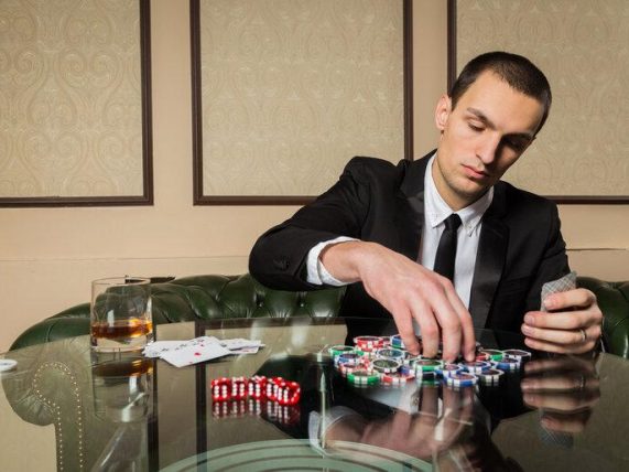 Man in a suit playing poker with chips and cards at a table, illustrating the journey from online gambling wins to withdrawal processing and payouts.