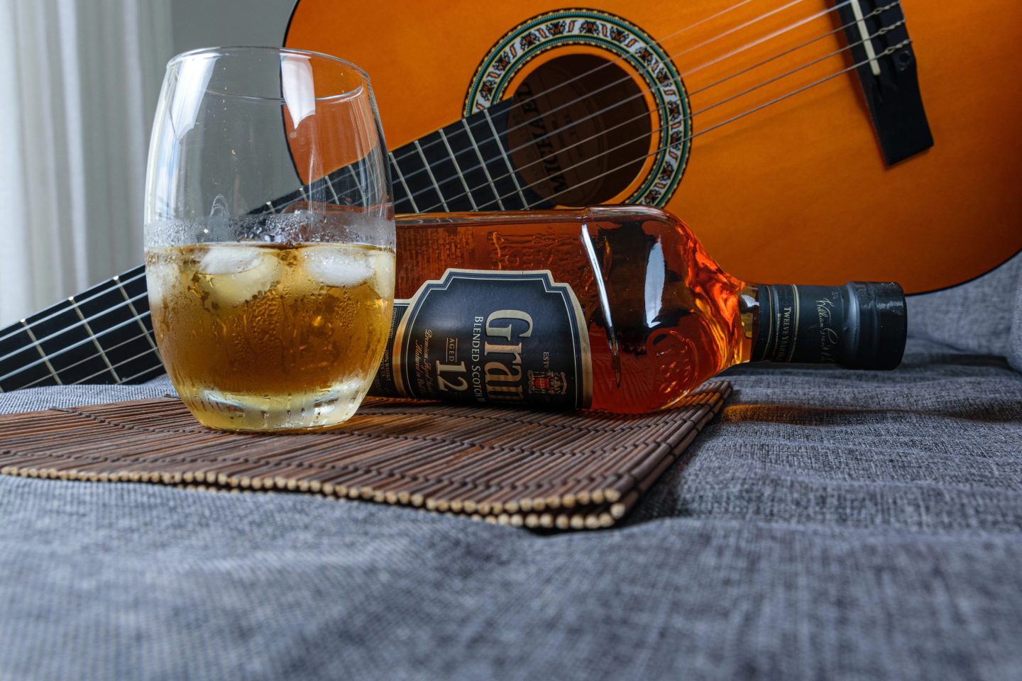 A glass of whiskey next to a bottle and a guitar for playing whiskey songs