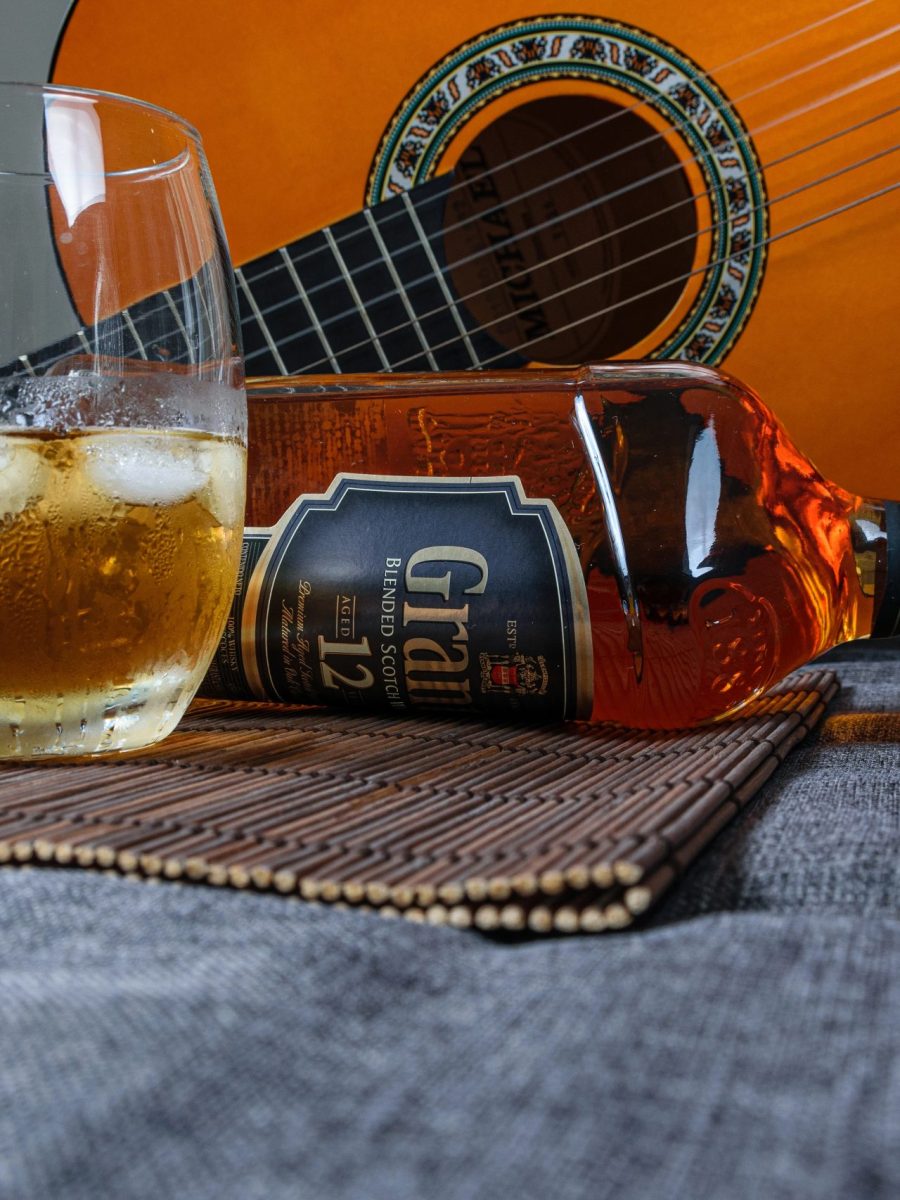 A glass of whiskey next to a bottle and a guitar for playing whiskey songs