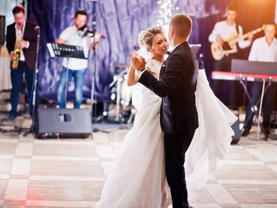 Bride and groom dancing at a wedding reception with a live band performing in the background.