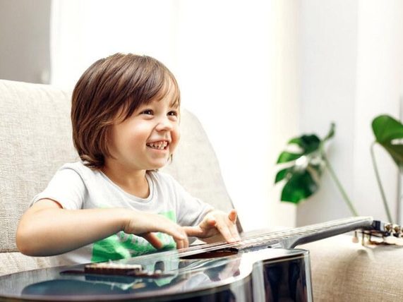 Child learning music at home while playing guitar. 
