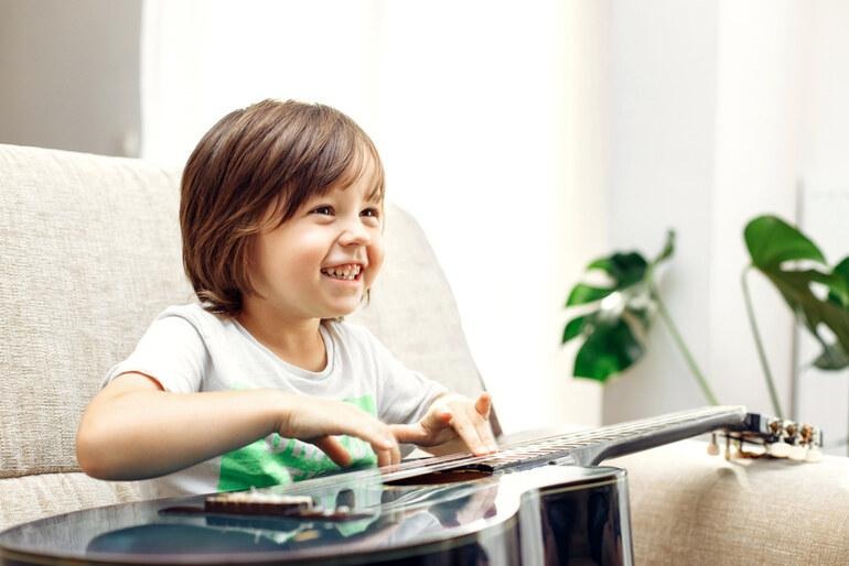 Child learning music at home while playing guitar.
