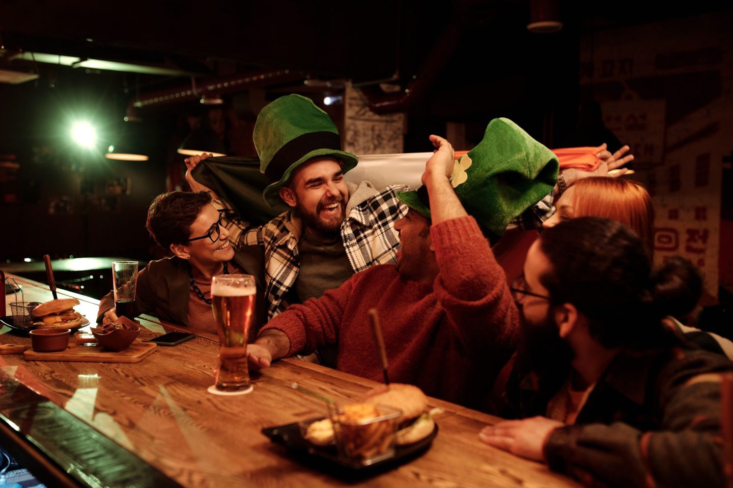 A group of people laughing at a bar with Irish hats on